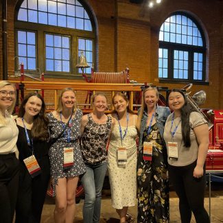CSTE AEF Class 20 - Maternal and Child Health (MCH) Fellow Cohort photo at the Heniz History Center in Pittsburgh, PA during the Class 20 graduation event held by CSTE during the 2024 CSTE conference. It includes, starting far left, Jessi McCluskey-Shuey, Alyssa Pochkar, Rebecca Bussa, Michelle Azar, Preciosa Martinez, Hannah Gorman, and Danielle Siwula.
